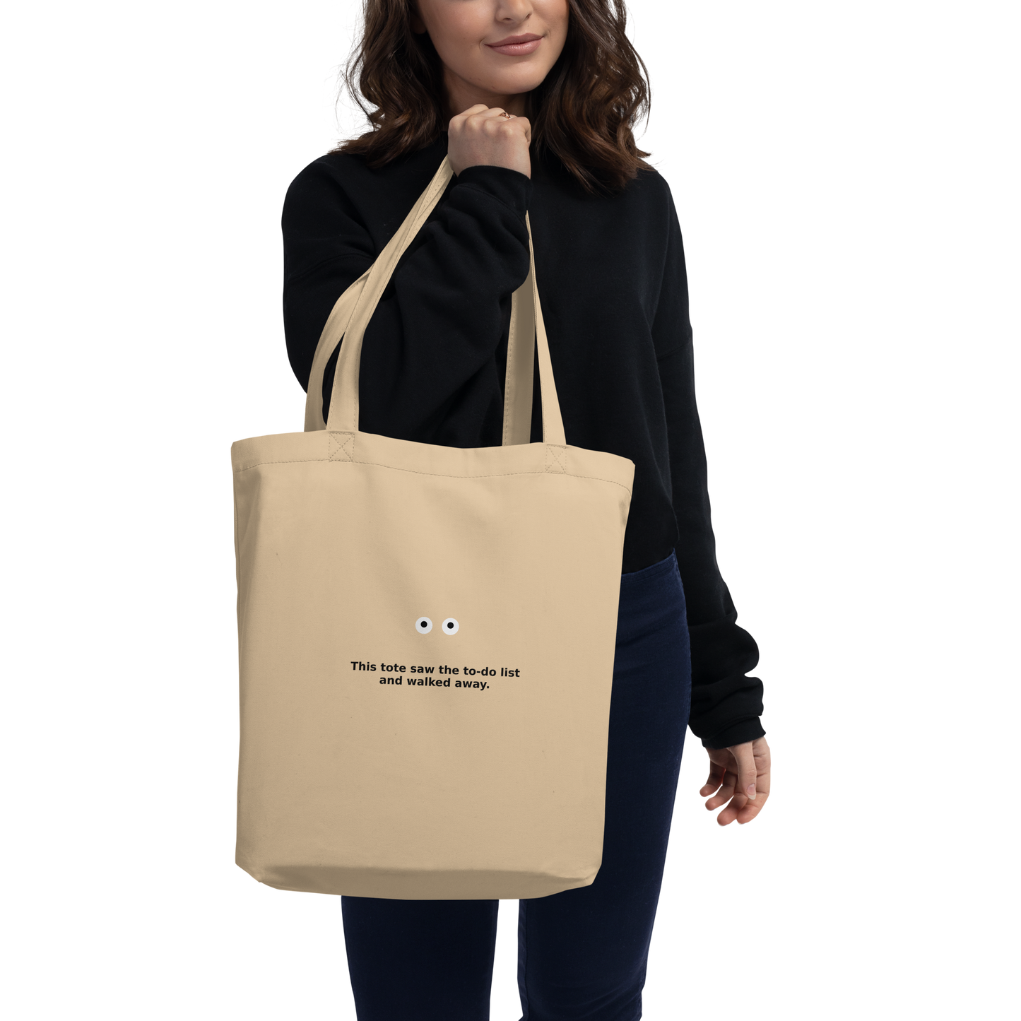 Model wearing a beige MISITIS™ tote with printed eyes and quote: “If I stare long enough, life might blink first.”
