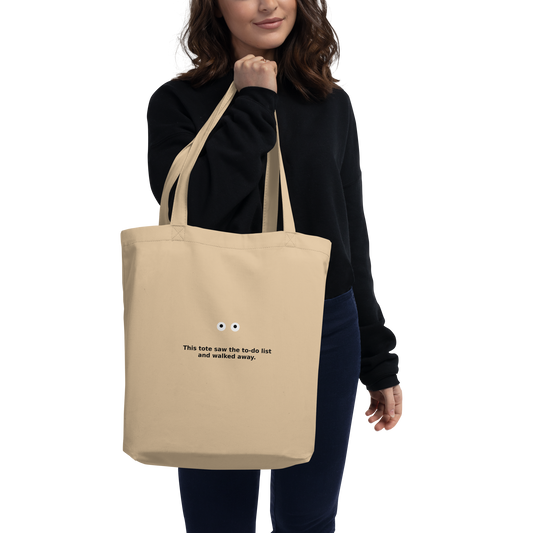 Model wearing a beige MISITIS™ tote with printed eyes and quote: “If I stare long enough, life might blink first.”
