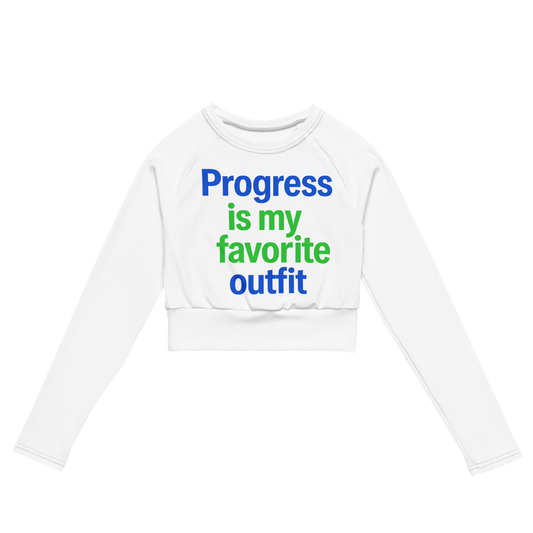 White cropped long sleeve shirt with colorful text reading “Progress is my favorite outfit” in blue and green.
