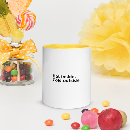White ceramic mug with yellow interior and printed text: “Hot inside. Cold outside.” Surrounded by candies and bright props.
