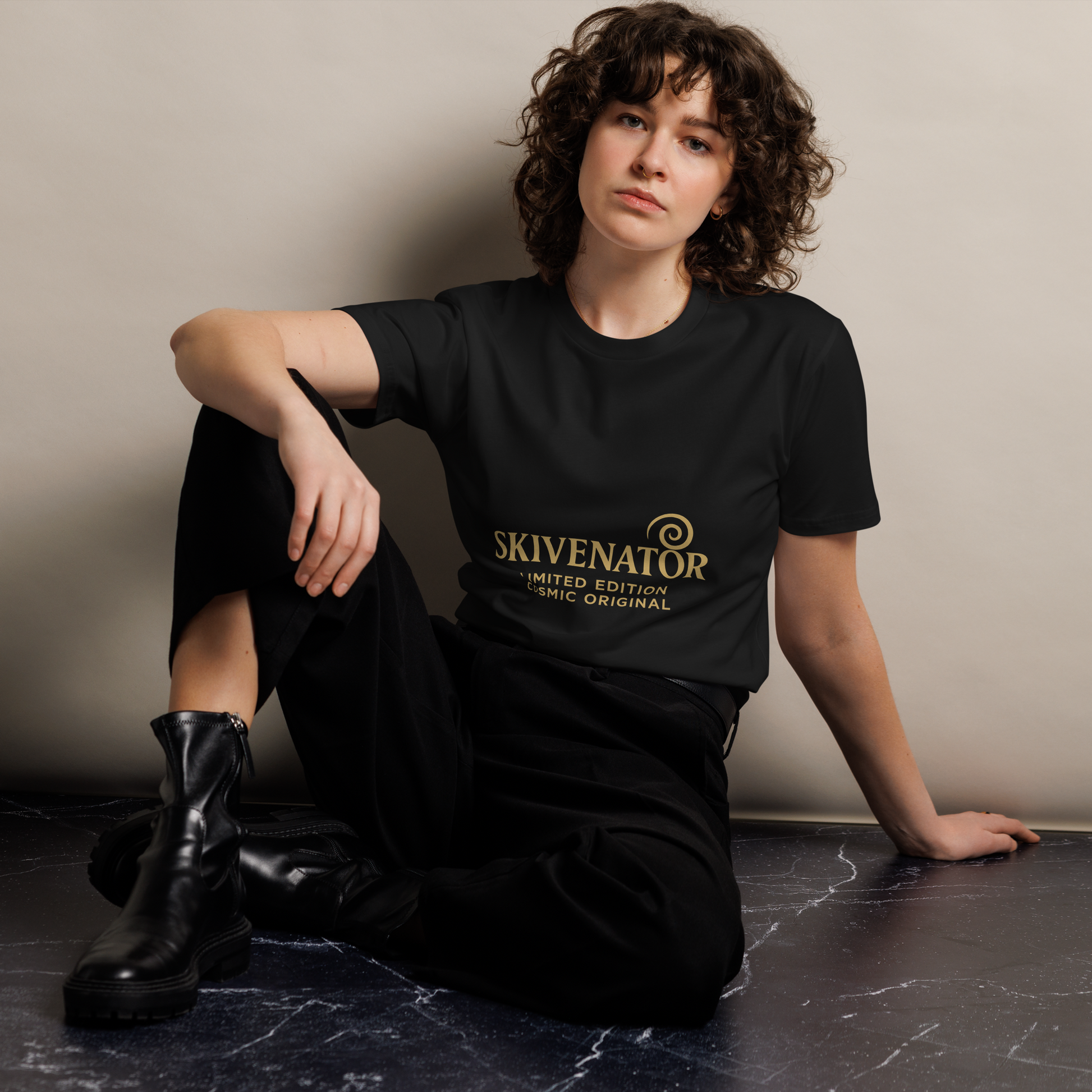 Black unisex t-shirt with gold SKIVENATOR logo and “Limited Edition Cosmic Original” text, worn by seated model against light backdrop.
