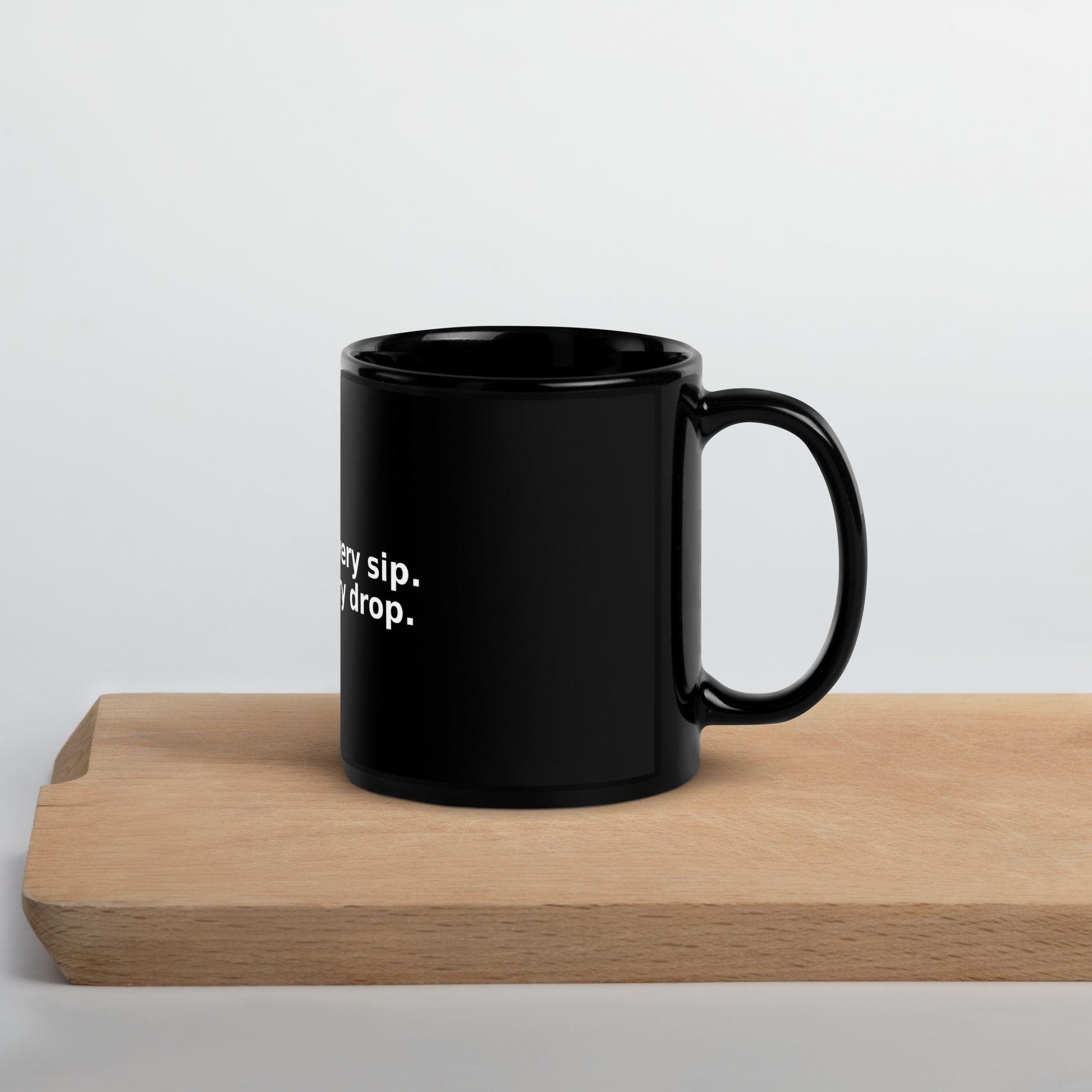 Glossy black ceramic mug on wood surface with white quote: “Grace in every sip. Wit in every drop.”
