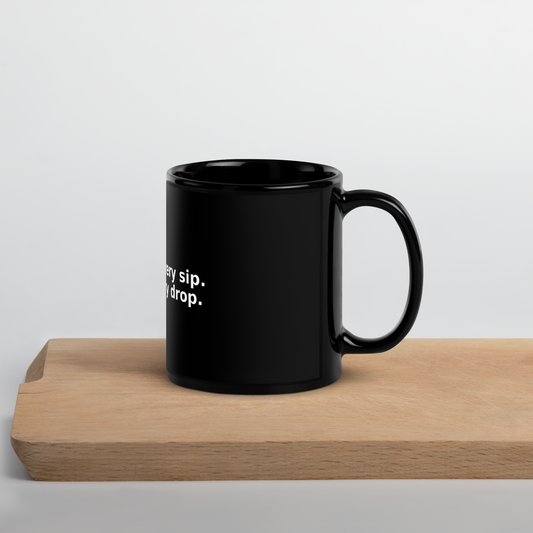 Glossy black ceramic mug on wood surface with white quote: “Grace in every sip. Wit in every drop.”
